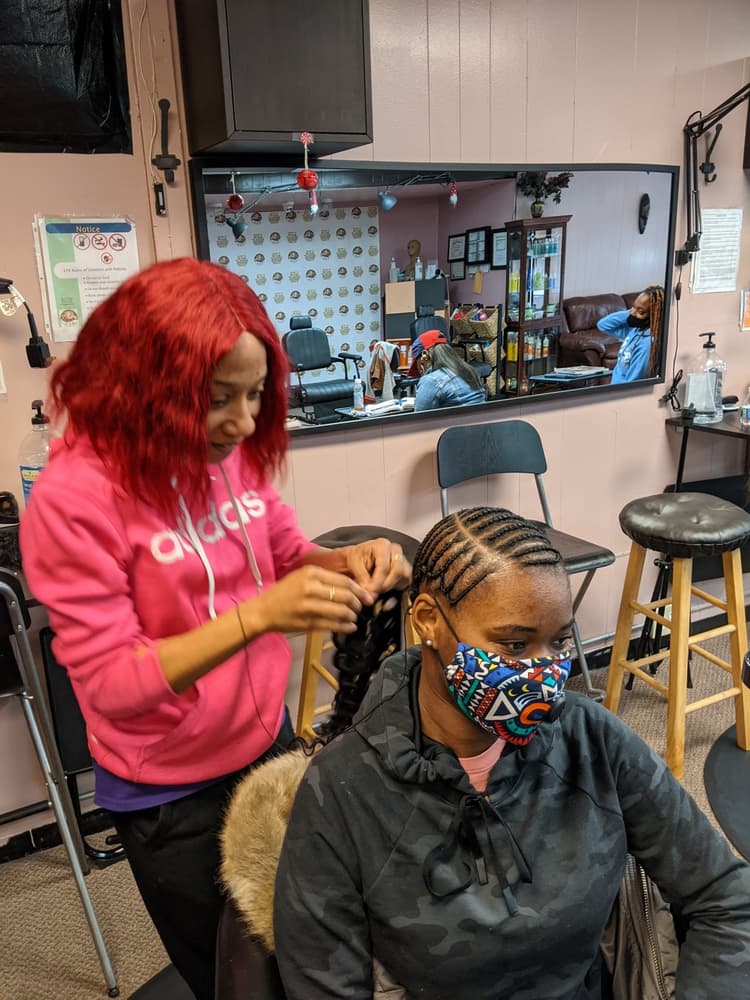 Student braiding cornrows on a live client under supervision